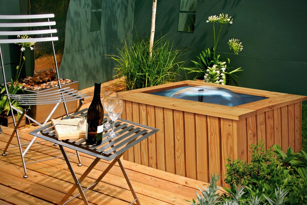 
			Bassin de terrasse carré en bois sur une terrasse en bois avec des meubles de jardin en métal.

		