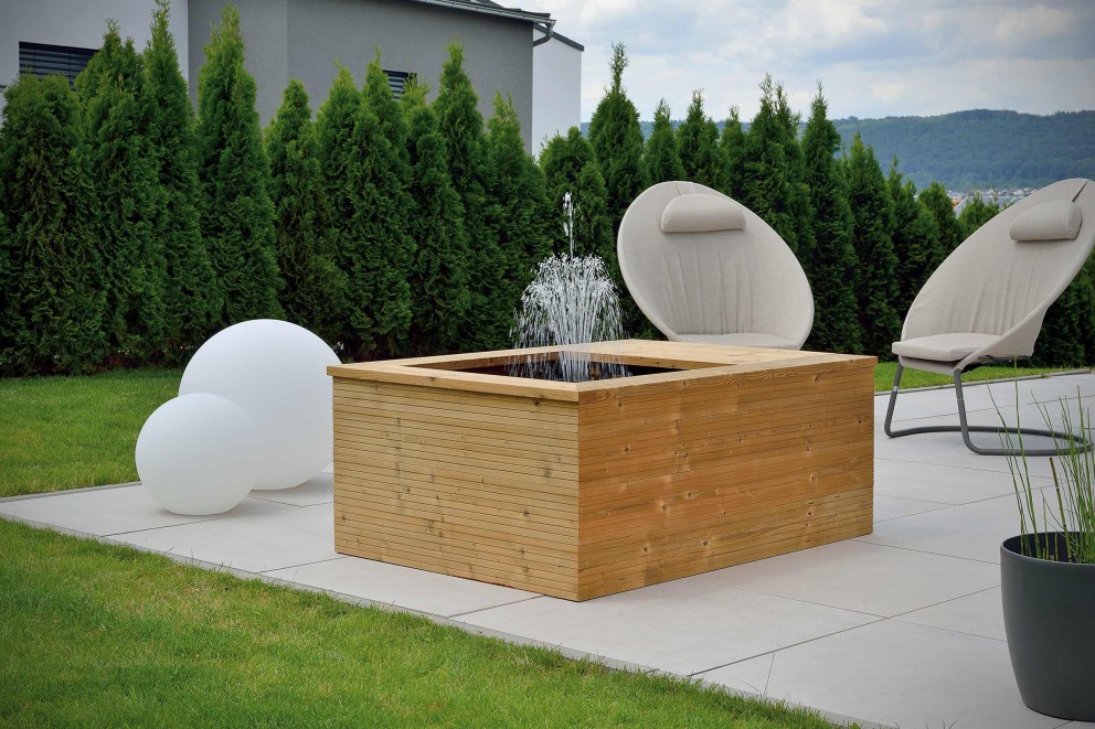 
			Bassin de terrasse rectangulaire avec une fontaine sur une terrasse carrelée avec des meubles de jardin et des sphères d&lsquo;éclairage.

		